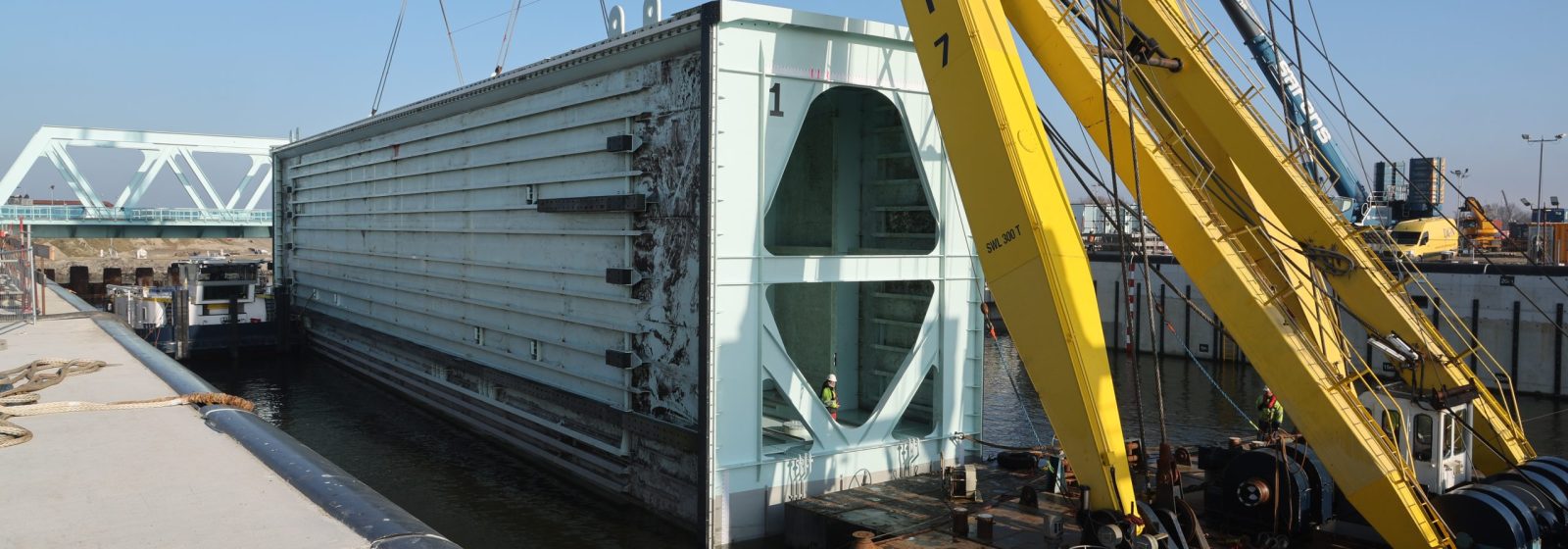 Aan de lieren van een hijsbok wordt de deur de sluiskolk ingevaren.