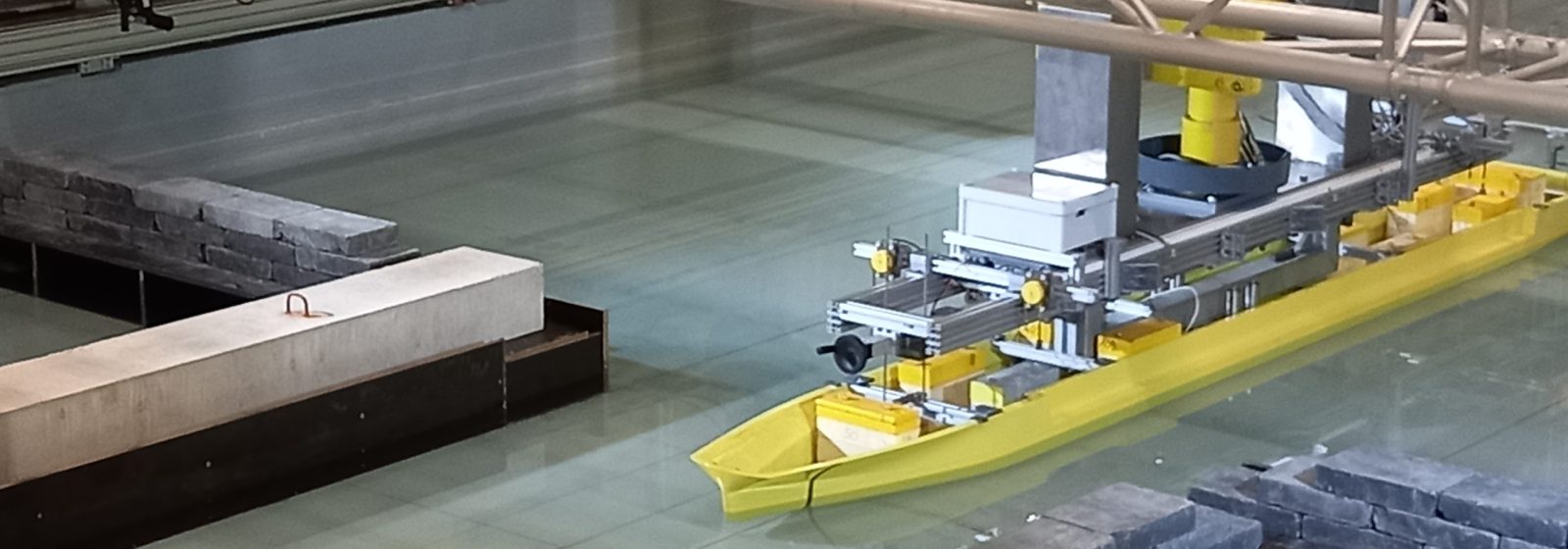 Het model van de X-Barge wordt voortbewogen door de sleepwagen in een gesimuleerd kanaal.